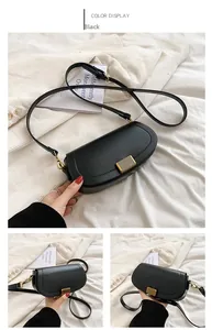 Detail of black semi-circular crossbody bag with textured gold clasp on white fabric