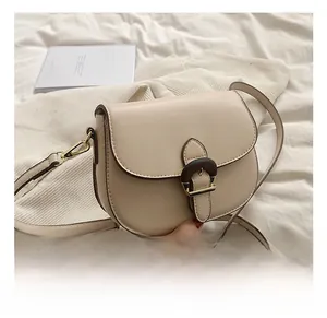 Detail showing the brown horseshoe buckle and golden hardware on a beige saddle bag