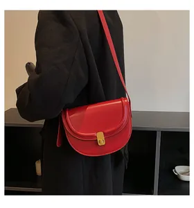Close-up of a red PU leather saddle bag with a gold buckle worn over a black coat