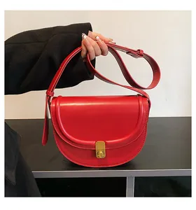 Close-up of a stylish red saddle bag with gold metal lock and matching shoulder strap