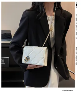 Detail of white quilted crossbody bag with gold lever lock and metal chain strap