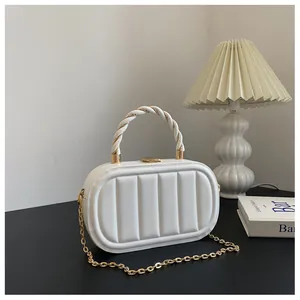 Détail d'un sac boîte blanc matelassé avec poignée tressée et bandoulière chaîne dorée