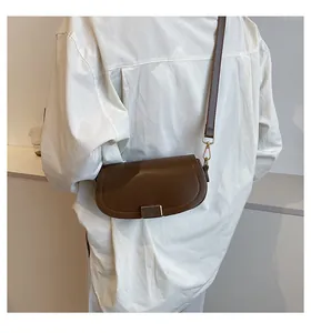 Brown leather saddle bag with gold hardware detail worn by model in a minimalist setting