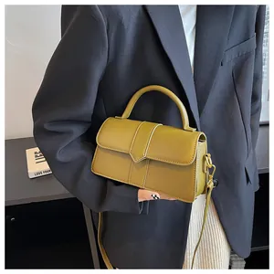 Detail of a mustard green crossbody bag with a triangular flap and top handle