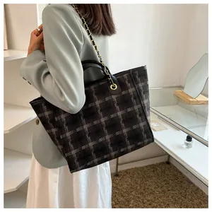 Large checkered tote bag with black leather trim and gold chain strap shown on model