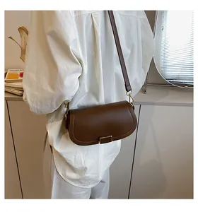 Detail view of a brown leather saddle crossbody bag with a gold rectangular metal clasp