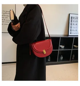 Chic red saddle shoulder bag with gold metal clasp on model in black coat
