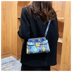 Detail shot of blue and yellow snakeskin crossbody bag with golden clasp on a model