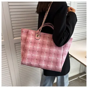 Detail of pink woven plaid tote bag featuring a metal chain strap and leather handle