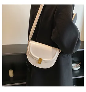 Close-up of cream PU saddle bag with gold metal lock on a black coat outfit