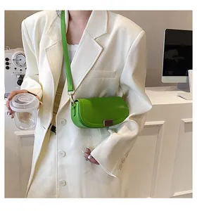 Detail of a bright green saddle bag with metal buckle worn over a beige blazer