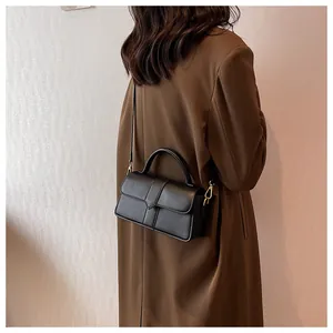 Close-up of a minimalist black rectangular leather handbag with gold metal hardware