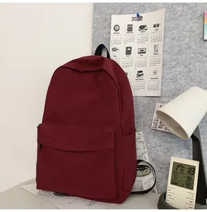 Detail view of large burgundy canvas backpack featuring front zip pocket in a study setting