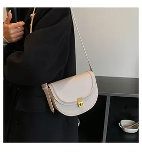 Model wearing a cream-white saddle bag with gold buckle and adjustable strap