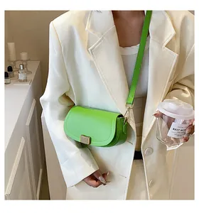 Detail of bright green mini saddle bag with metal buckle worn over a white blazer