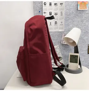 Side view of burgundy nylon backpack featuring side pocket and front zipper compartment