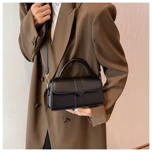 Detail of minimalist black handbag showing matte texture and silver triangular buckle
