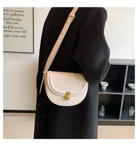 Side view of a cream PU leather saddle bag with gold buckle on a model in a black coat