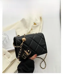 Detail view of black quilted shoulder bag featuring gold chain and small ball ornament