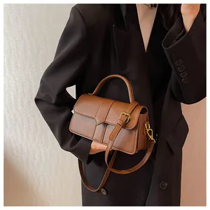 Detail of dark brown leather handbag featuring a curved handle and golden metal buckles