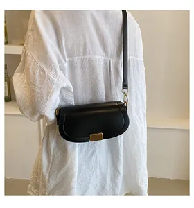 Model wearing a black crossbody bag with gold buckle over a white shirt, detail view