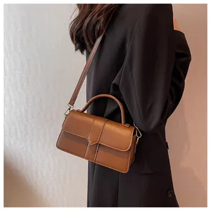 Detail view of deep brown leather crossbody bag featuring gold hardware and top handle