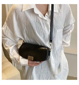 Detail shot of a black crescent crossbody bag with gold buckle on a white blouse