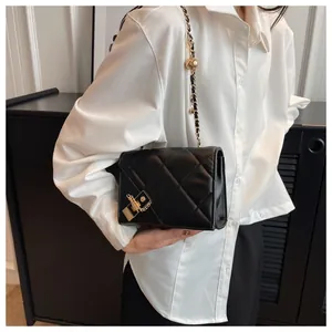 Detail of black quilted crossbody bag with gold chain strap and metal lock closure