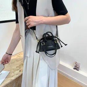 Mini black crossbody bag with drawstring closure and top handles worn by a model