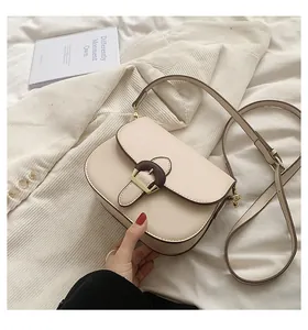 Detail of cream saddle bag with wood grain buckle and dark brown oil edges on white fabric