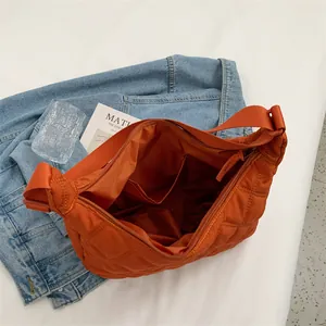 Orangefarbene Stepptasche aus Nylon mit Rautenmuster und verstellbarem Gurt auf weißem Grund