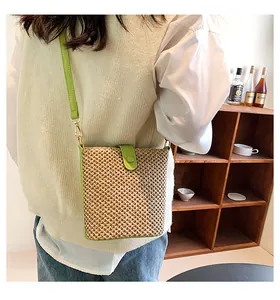 Detail of woven straw crossbody bag with vibrant green leather trim and golden hardware