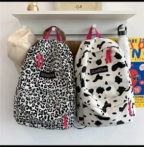 Détail de sacs à dos en toile léopard et vache avec sangles roses sur mur blanc