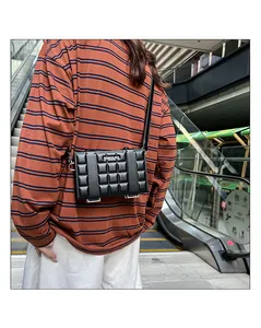 Close-up of a black quilted crossbody box bag on a person in an outdoor setting