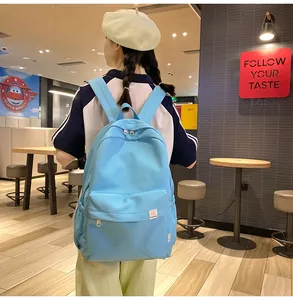 Rear view of model wearing a light blue large capacity student backpack in a modern cafe