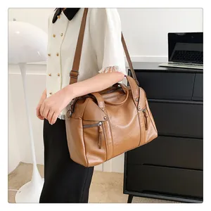 Detail of camel Boston bag with decorative zippers, tassels, and adjustable shoulder strap