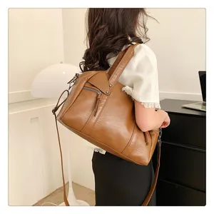 Caramel brown leather Boston bag with tassel detail worn by model in cozy indoor setting