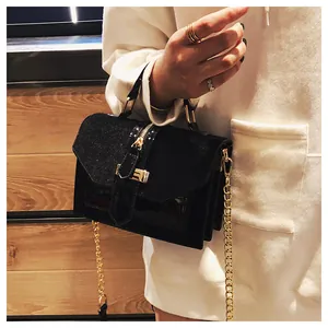 Detalle de bolso negro bandolera en ante con cadena dorada y cierres metálicos elegantes