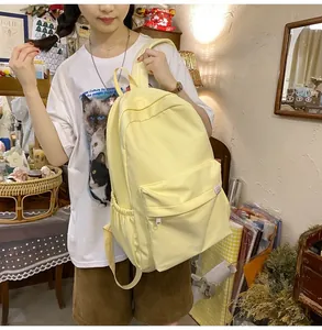 Detail of a light yellow canvas backpack showing the multi-pocket structure on a model