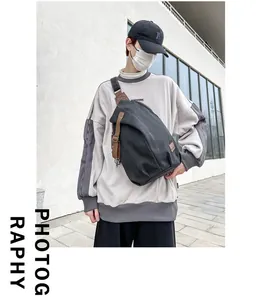 Detail view of large black canvas crossbody bag with vintage brown leather accents on a model