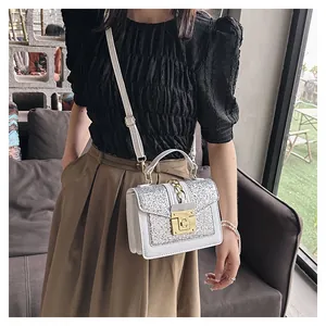 Close-up of white crossbody bag with silver sequins and gold metallic lock detail