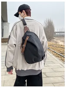Close-up of black canvas sling bag with brown leather details worn on the back outdoors