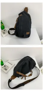 Detail of black canvas crossbody bag with brown leather brand tag and metal buckle