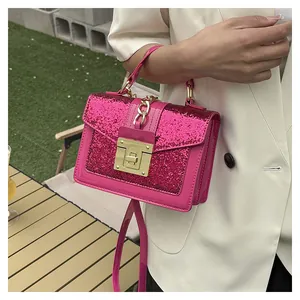 Detail of a bright pink sequined square bag with gold metal lock and chain strap