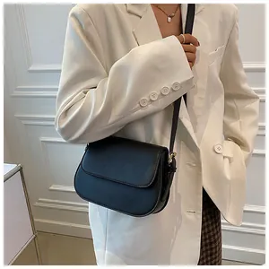 Detail of minimalist black matte leather saddle bag with gold buckle on white blazer