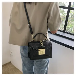 Detail of black glitter flap bag with gold square buckle and chain handle on model