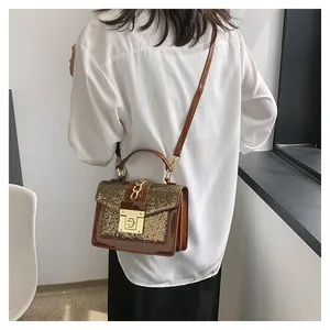 Detail of dark brown sequin and patent leather crossbody bag with gold hardware buckle