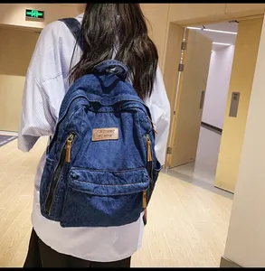 Detail van blauwe denim rugzak met leren patch en ritszakken gedragen door een model