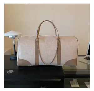 Detail of beige canvas tote bag with brown leather trim and metal chain on a black table