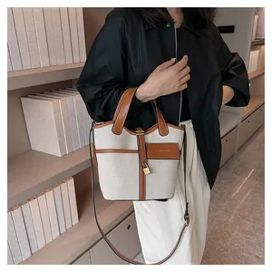 Chic beige canvas bucket bag with brown leather trim shown on a model in a library